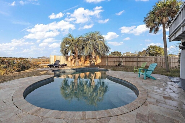 A backyard with a swimming pool, palm trees, and outdoor furniture.