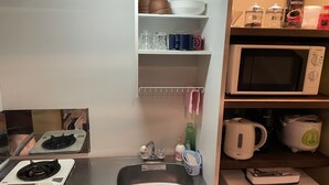 A compact kitchen with a stove, sink, microwave, and shelves with dishes and kitchenware. - Kanon House (Kyoto)