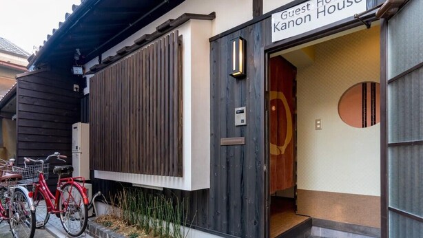 A guest house entrance with a wooden door, a sign reading "Guest House Kanon House," and bicycles parked outside. - Kanon House (Kyoto)