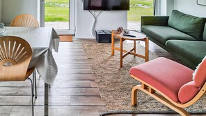 Een moderne woonkamer met een houten vloer, een groene bank, een rode fauteuil en een aan de muur bevestigde televisie.
