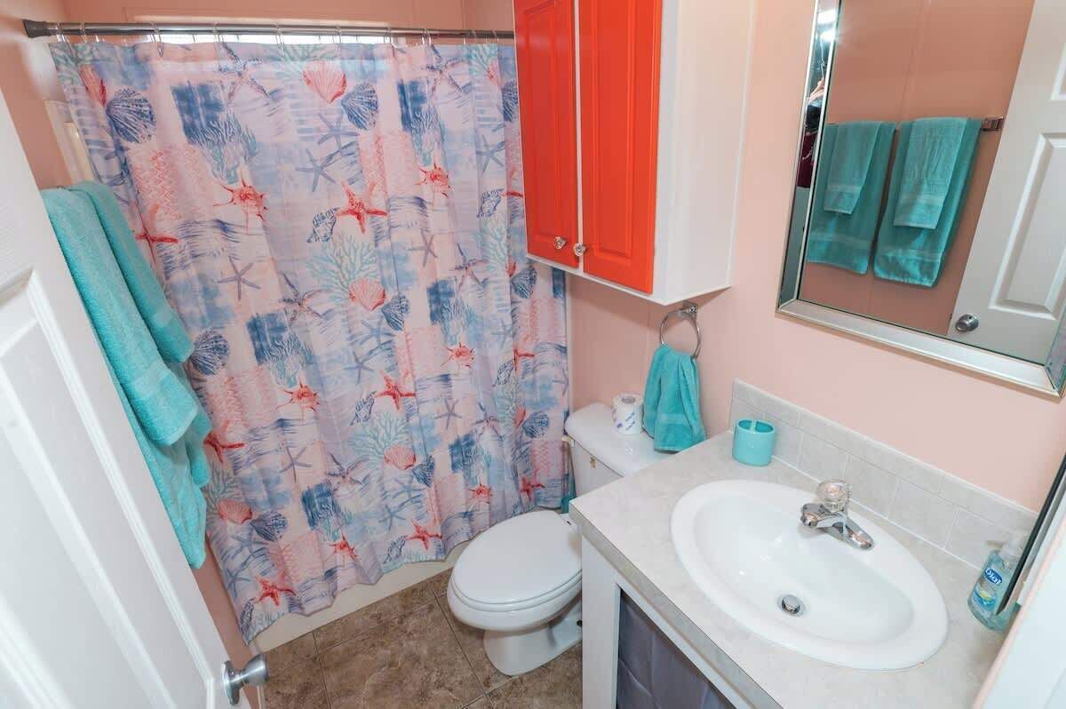 Une salle de bain équipée d’un rideau de douche orné d’un motif représentant la vie marine, de toilettes, d’un lavabo avec un miroir au-dessus et d’un porte-serviettes avec une serviette.