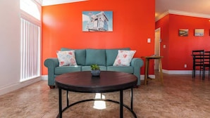 Un salon avec un canapé de couleur turquoise, une table basse ronde et un tableau représentant un camion accroché au mur.