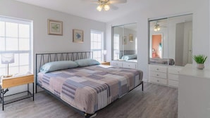 Une chambre à coucher comprenant un lit, une table de chevet, une commode et un grand miroir.
