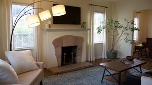 A living room with a fireplace, a sofa, a coffee table, and a potted plant. - The Tudor Rose - A classy, comfortable getaway (San Anselmo)