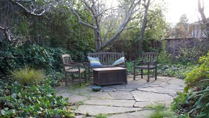 A patio with stone flooring, wooden furniture, and lush greenery. - The Tudor Rose - A classy, comfortable getaway (San Anselmo)