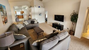 Un salon moderne avec un canapé d’angle gris, une table basse, un téléviseur et un ventilateur de plafond.