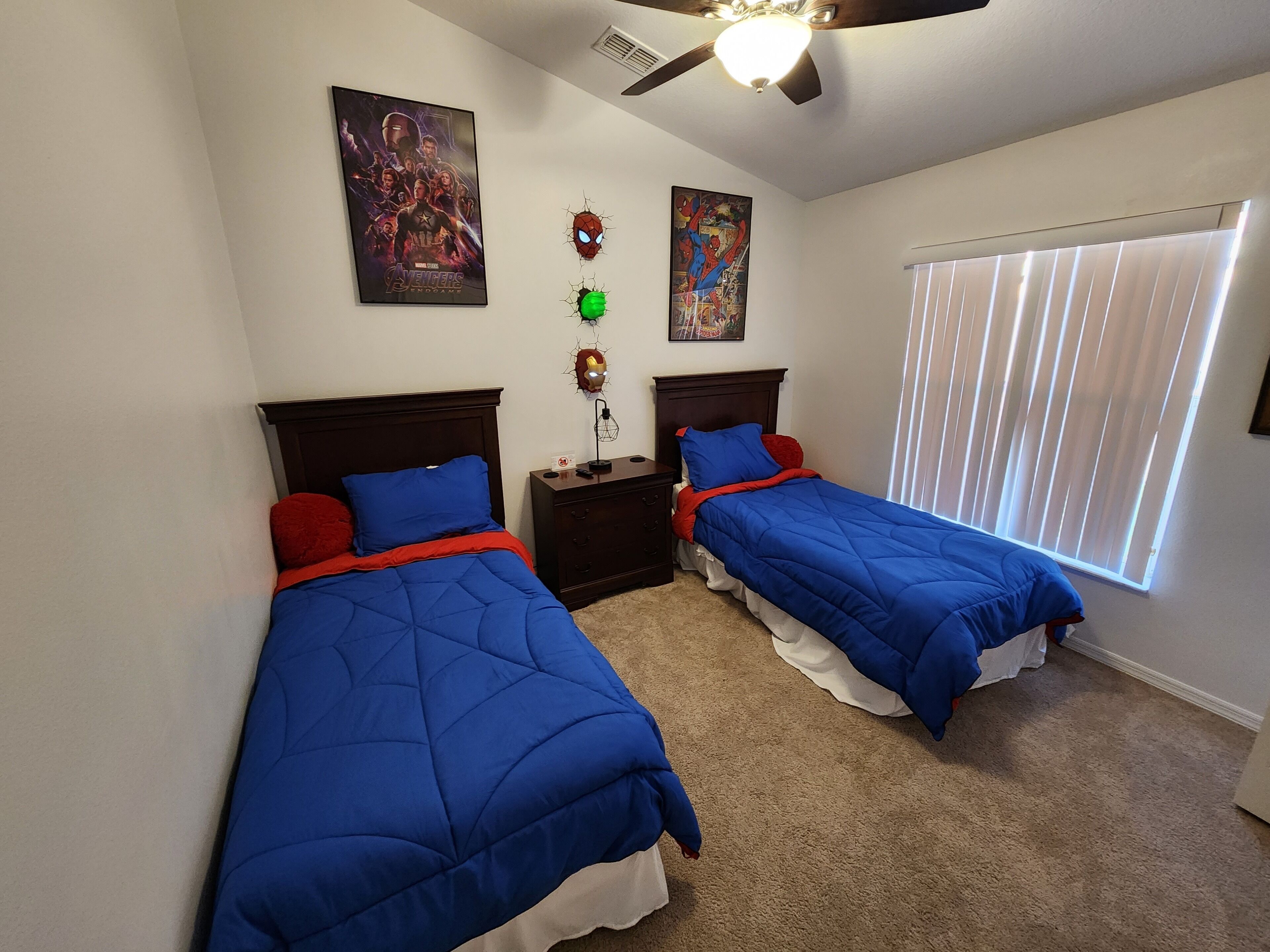 Ein Schlafzimmer mit zwei Betten, jeweils mit blauer Bettwäsche und roten Kissen, einem Deckenventilator und einem Fenster mit Jalousien.
