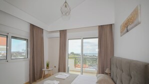A bedroom with a bed, a small table with a plant, and a view of the outside. - Piccolo Paradiso Villa A (Lachania)