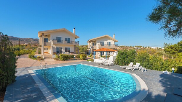 A swimming pool with lounge chairs, a covered seating area, and two large houses with balconies. - Piccolo Paradiso Villa A (Lachania)