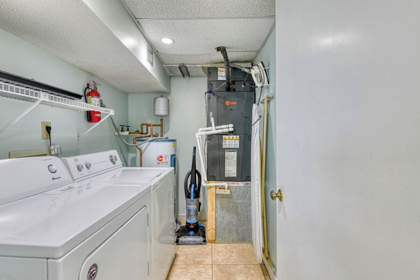 A laundry room with a front-loading washer, a water heater, and a vacuum cleaner.