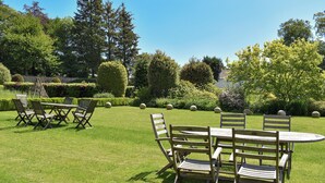 Un jardin agrémenté d’une table et de chaises en bois, entouré de haies et d’arbres bien entretenus.