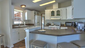 A kitchen with white cabinets, a central island with stools, a stove, microwave, and a sink. - Alpaca My Bags & Alpaca Experience! (Silt)