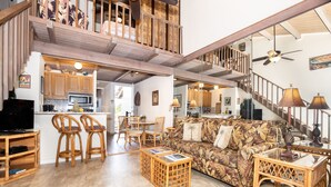 A spacious living area with a high ceiling, wooden furniture, and a staircase leading to an upper level.