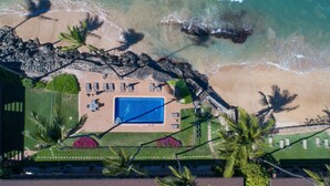An aerial view of a resort with a swimming pool, beach, and palm trees.