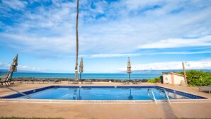 A swimming pool with lounge chairs and umbrellas, overlooking a beach and ocean.
