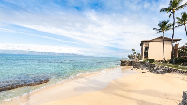 A beach with clear turquoise water, a sandy shore, and a building with balconies overlooking the ocean.