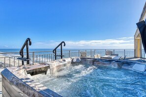 A hot tub with a view of the ocean, surrounded by lounge chairs and a railing.