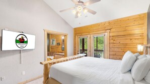 Un dormitorio con una cama grande, paredes de madera, un ventilador de techo y un televisor mostrando un logotipo.