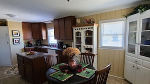 A kitchen with wooden cabinets, a dining table with chairs, a vase with flowers, and a window with blinds. - House on the Hill - 5 Beds, 2 Baths Near Downtown Zebulon (Zebulon)