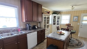 A kitchen with dark wooden cabinets, a dishwasher, a granite countertop, a sink, and a trash bin. - House on the Hill - 5 Beds, 2 Baths Near Downtown Zebulon (Zebulon)