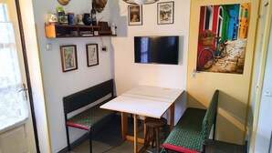 Ein Zimmer mit einem Tisch, zwei Bänken, einem Fernseher, Wanddekorationen und einer Tür mit einem farbenfrohen Wandgemälde.