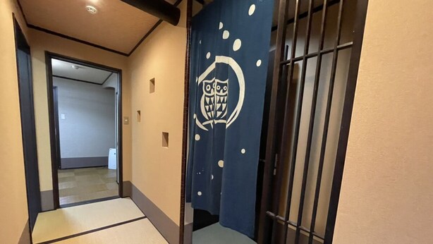 Un passadís amb estores de tatami, una porta corredissa amb un dibuix blau i una reixa metàl·lica.