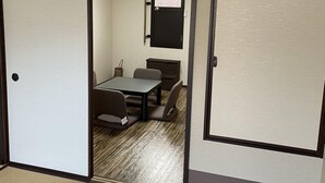 Una habitació amb paviment de tatami, una taula baixa amb cadires i una porta corredissa que dona a una altra habitació.