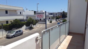 A view from a balcony overlooking a street with a supermarket sign, buildings, and a car. - Central apartment just steps from the beach with balcony (San Foca)