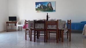 A dining area with a table set for two, a television on a stand, and a painting of a coastal landscape on the wall. - Central apartment just steps from the beach with balcony (San Foca)