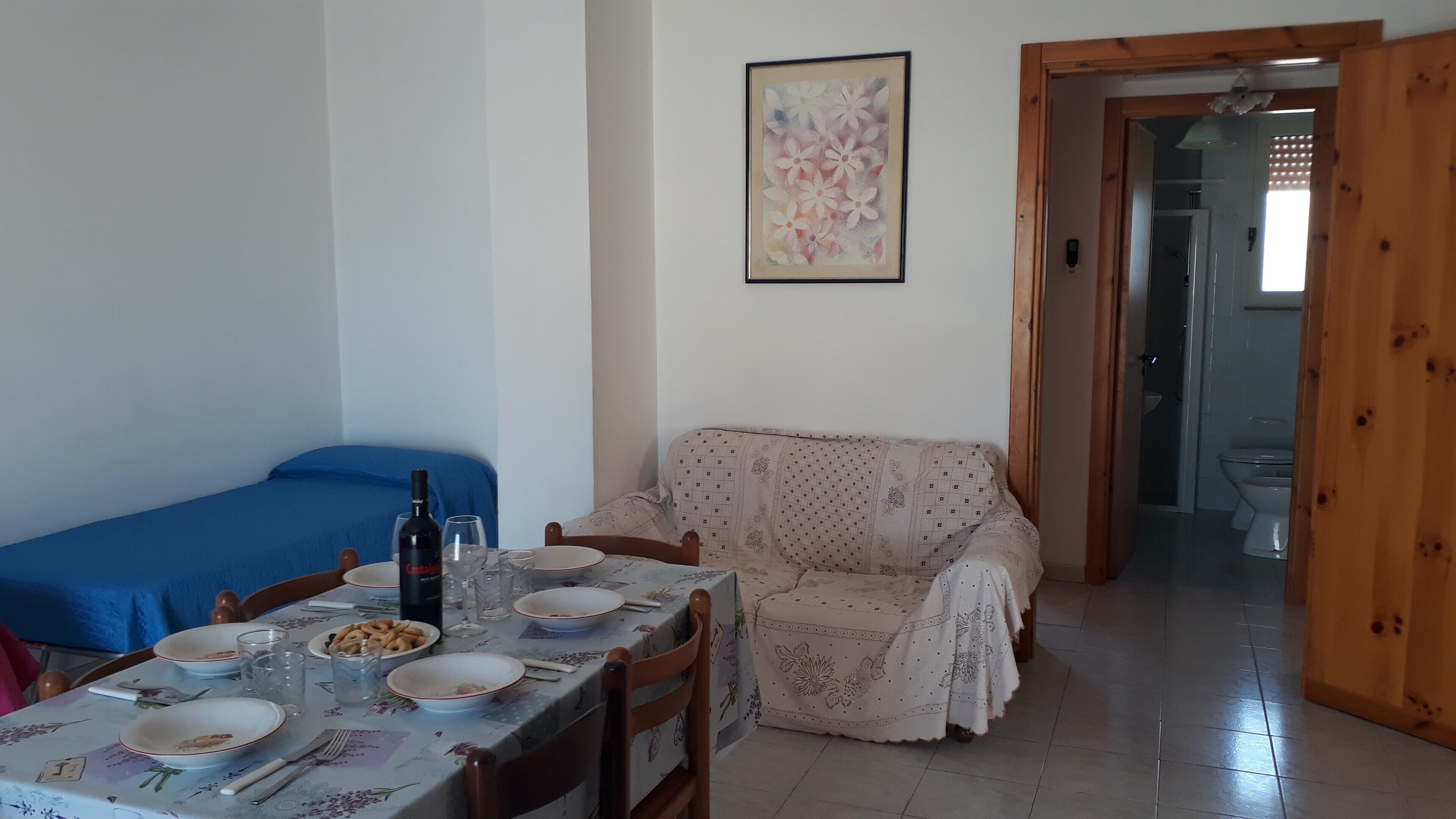 Ein Essbereich mit Tisch für zwei Personen, einer Couch, einem Gemälde an der Wand und einer Holztür, die ins Badezimmer führt.