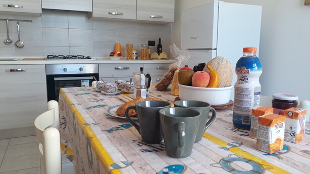 A kitchen with a table set for breakfast, including bread, fruits, and beverages. - Central apartment just steps from the beach with balcony (San Foca)