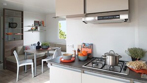 A modern kitchen with a gas stove, a dining area with a table and chairs, and a view of greenery outside.