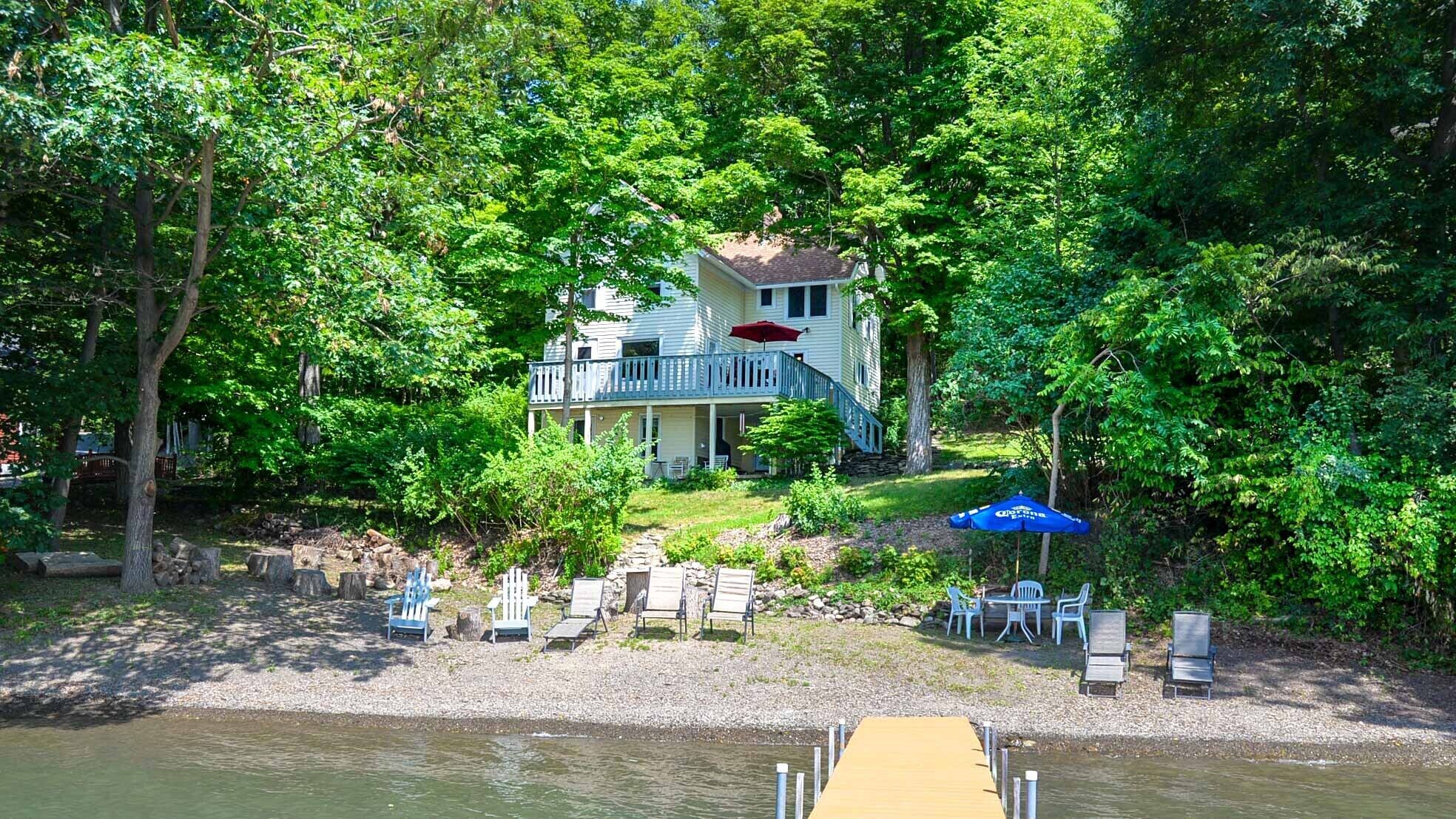 A lakeside cabin with a deck, outdoor seating, and a dock.