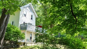 Una casa a due piani con un balcone, circondata da alberi verdi e rigogliosi.