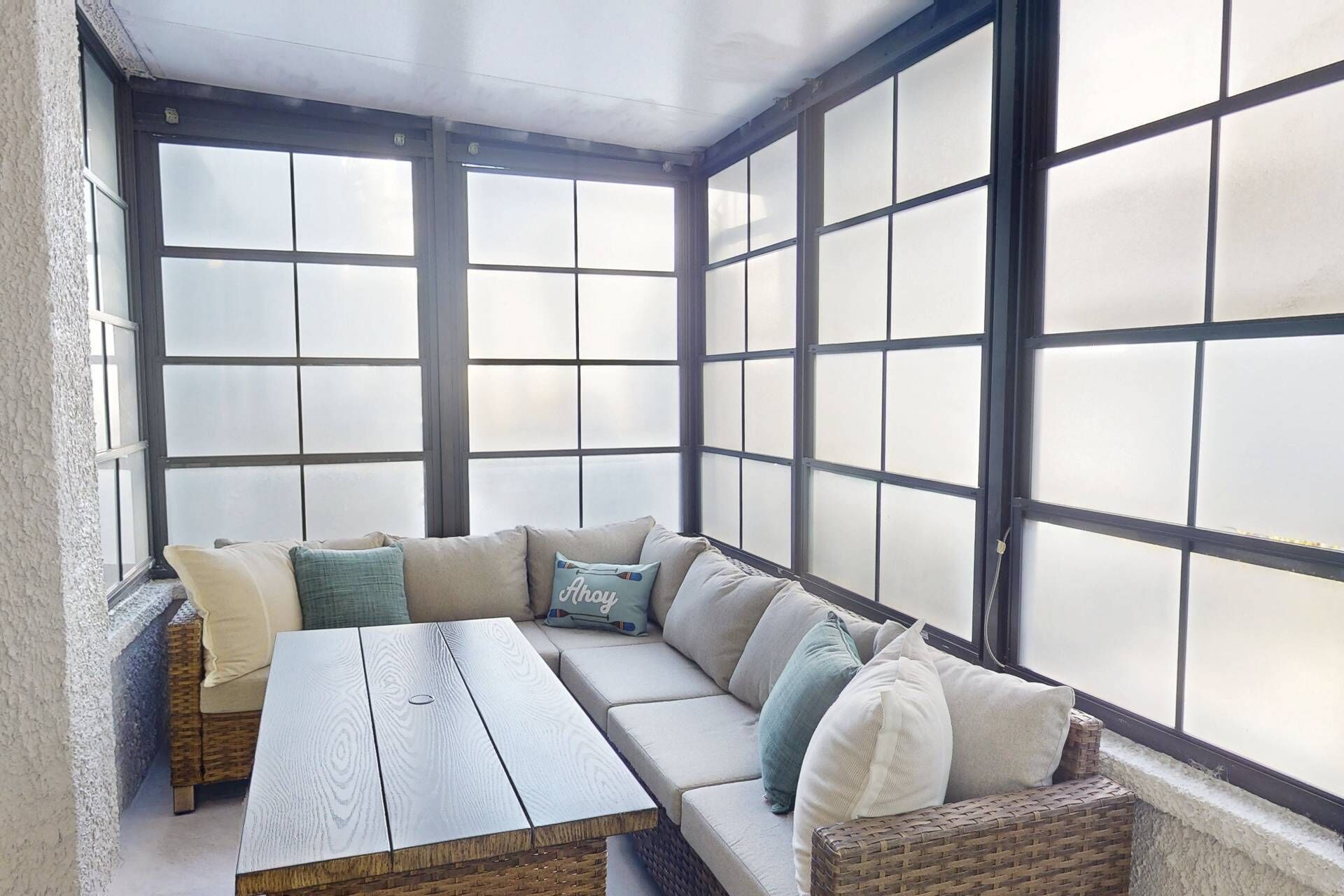 A sunroom with a large window, a wooden table, and a cushioned seating area.