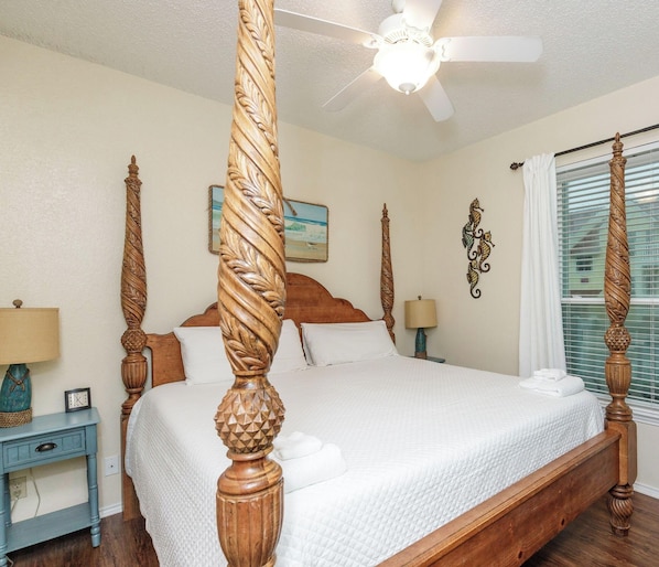 A clean, well-maintained bedroom with a four-poster bed, a ceiling fan, and a window with blinds.