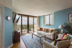 Un salón con sofá, mesa de centro y televisor. Tiene un balcón con vistas.