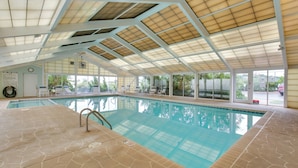 Una piscina interior con suelo de baldosas, paredes de vidrio transparente y techo con tragaluces.