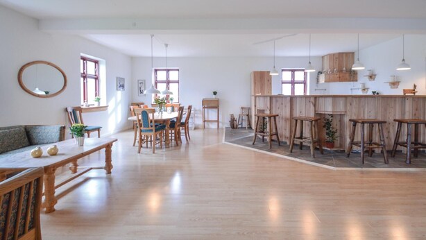 Een ruime kamer met een houten eettafel, stoelen, een bank en een bar met krukken.