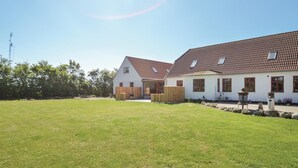 Een wit gebouw met een rode dakbedekking, een houten hek en een verzorgd gazon.