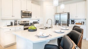 A modern kitchen with white cabinetry, stainless steel appliances, a central island with seating, and pendant lighting.