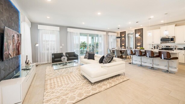 A modern living room with a white sofa, a glass coffee table, and a kitchen area with white cabinets and a dining table.