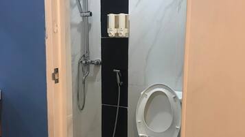 Un baño con inodoro, ducha con cabezal de ducha manual y dispensador de jabón de pared.