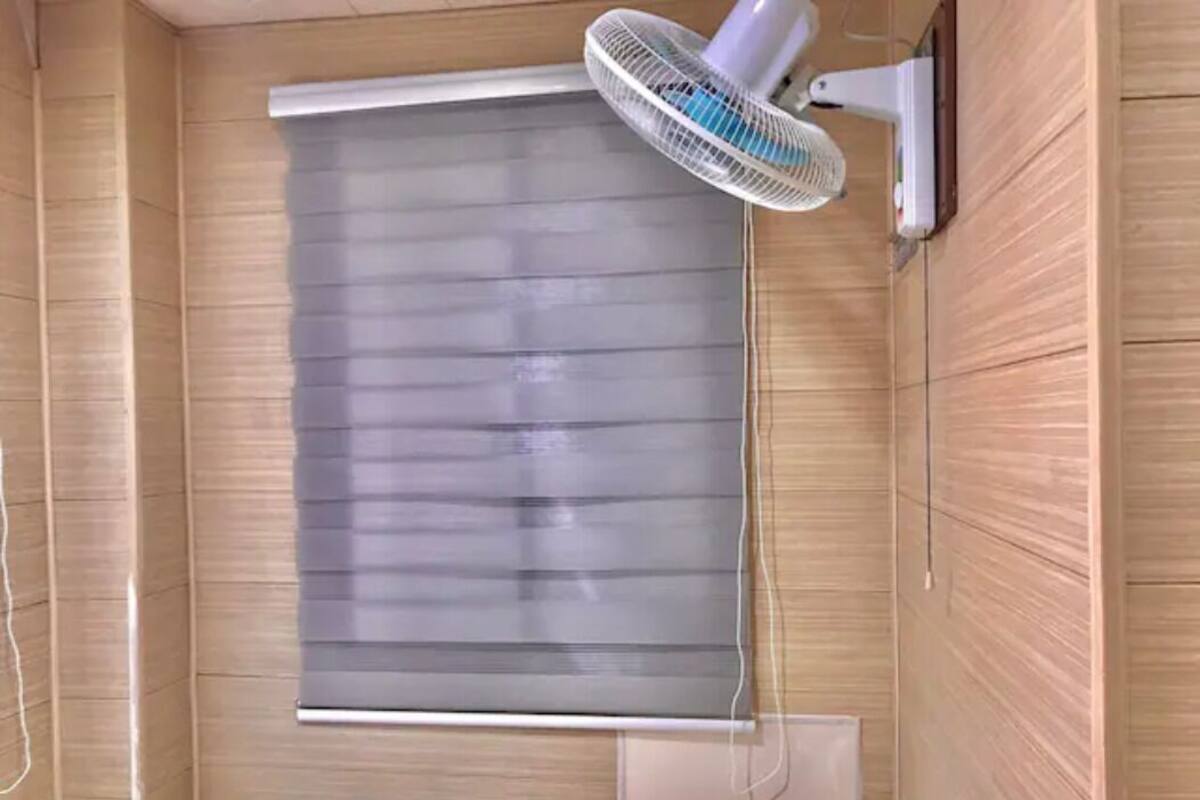 Een kamer met een groot raam voorzien van zonwering, een ventilator en een klein tafeltje.