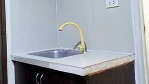Een keuken met een wit aanrecht, een gele kraan en donkerhouten kastjes.