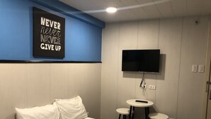 Een hotelkamer met een bed, een aan de muur bevestigde televisie en twee kleine tafels.