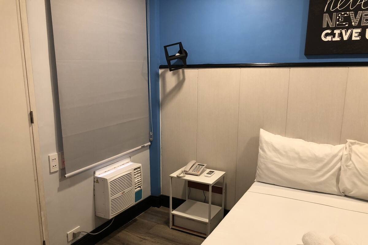 Een hotelkamer met een bed, een nachtkastje met een telefoon, een wandheater en een motiverende quote op de muur.