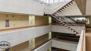 Un interior de varios niveles con una escalera central, señales de salida de emergencia y un techo de cristal.