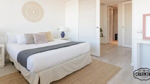 Un dormitorio con cama, mesitas de noche, decoración en la pared y una puerta que da a otra habitación.