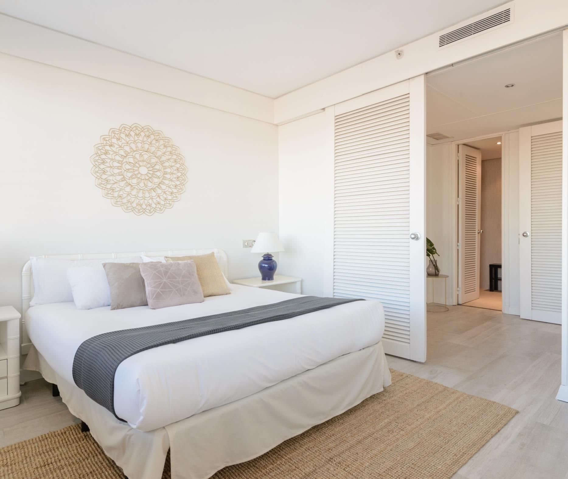Een slaapkamer met een bed, nachtkastjes, wanddecoratie en een deur naar een andere kamer.